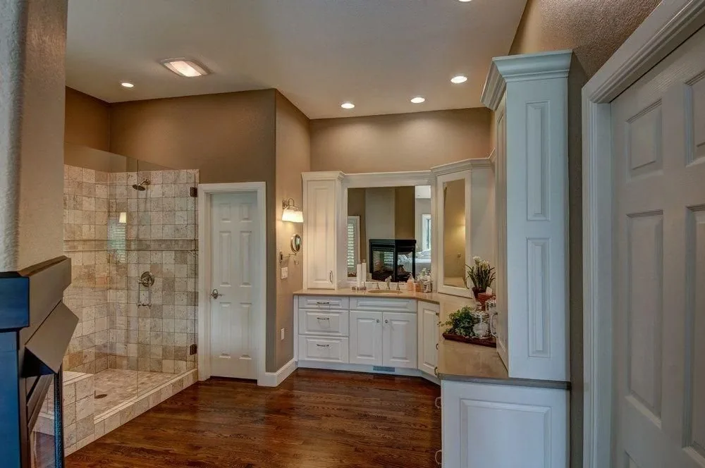 A Plush Designs bathroom with a tiled shower, light cabinetry and a framed mirror