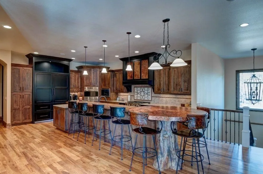 A Plush Designs kitchen with a long island, dark cabinetry and pendant lighting