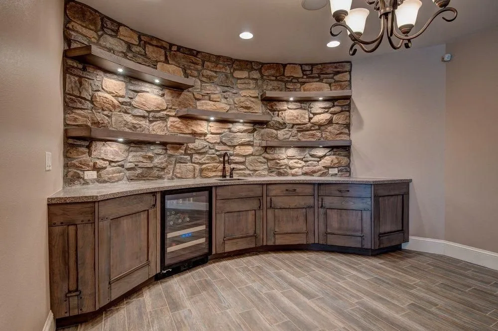 Home bar by Plush Designs, with a curved counter, stone wall and wine refrigeration