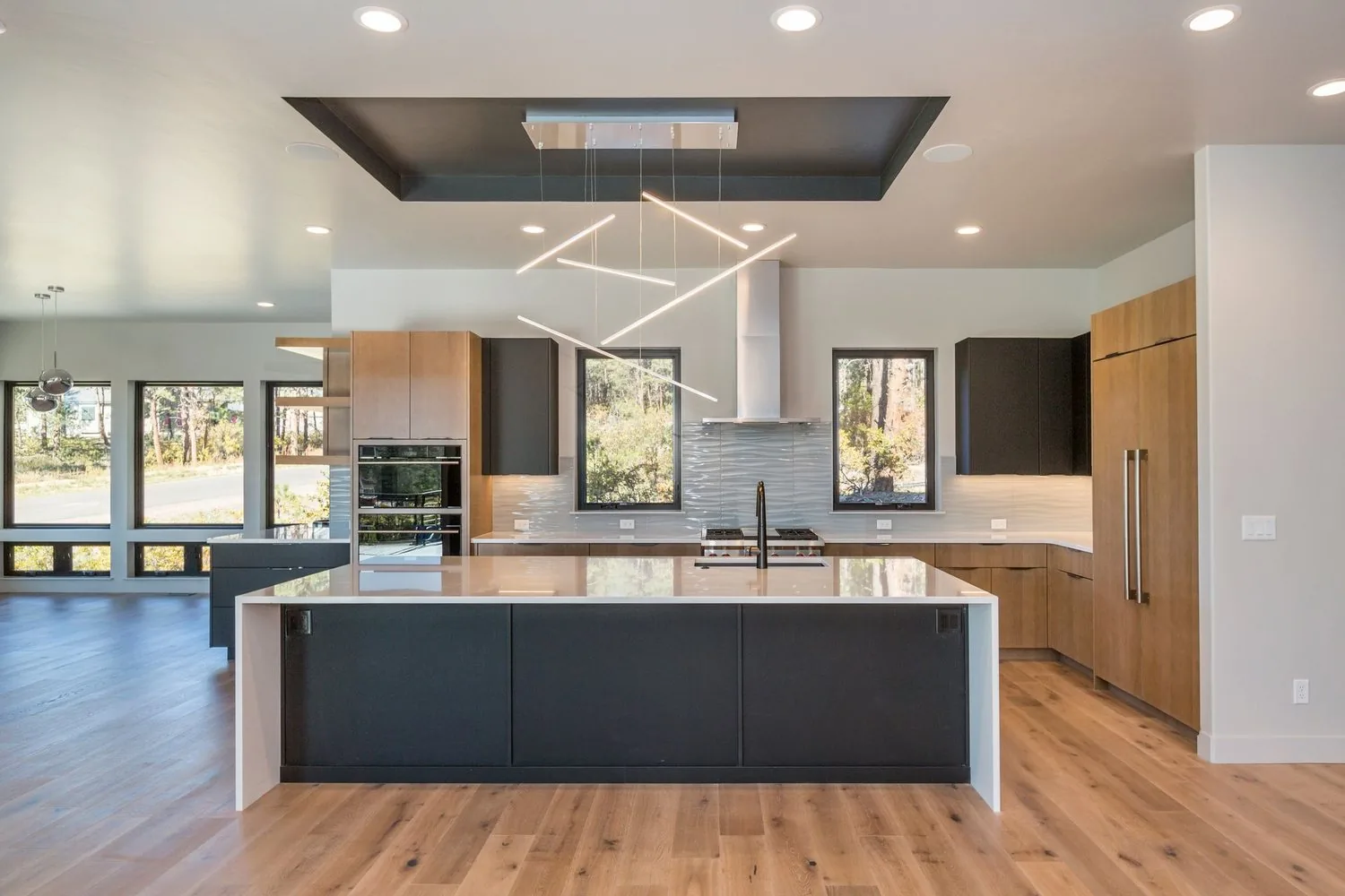 Copper Valley Kitchen by Plush Designs, with a dark island, pale counters and linear pendant lighting